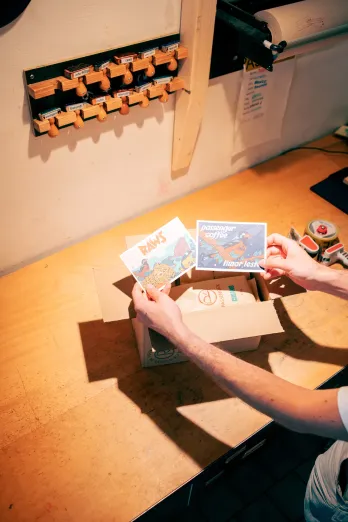 Postkarten werden zum Probierpaket in den Versandkarton gelegt